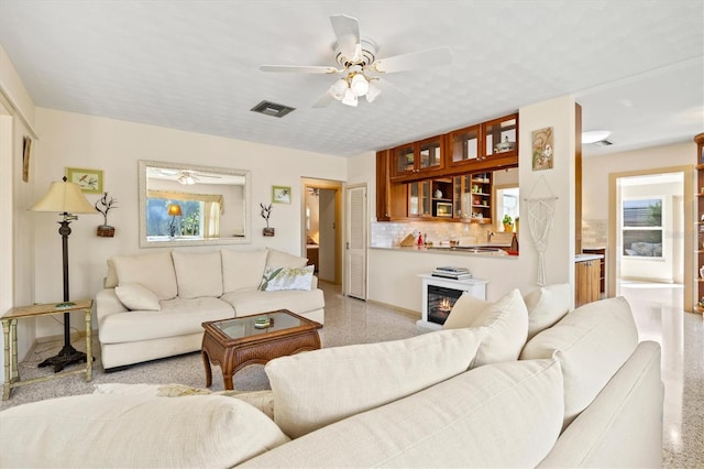 living area with baseboards, visible vents, light speckled floor, and ceiling fan