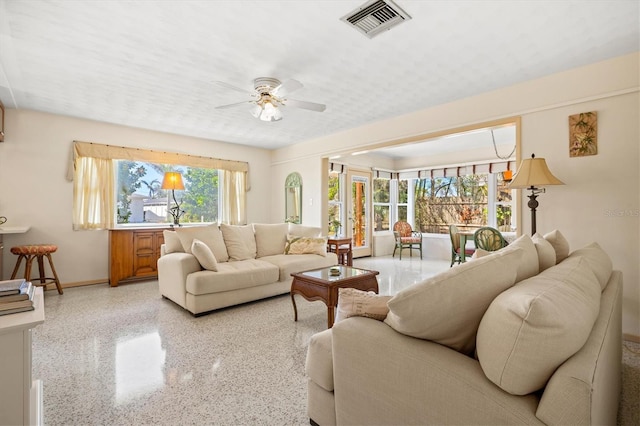 living area with visible vents, baseboards, speckled floor, and a ceiling fan