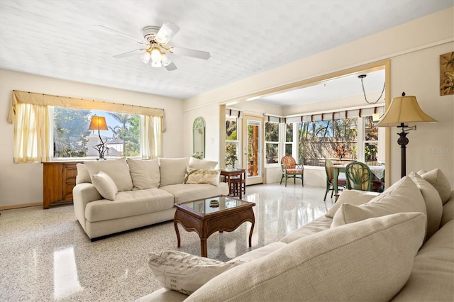 living area featuring light speckled floor, baseboards, and a ceiling fan