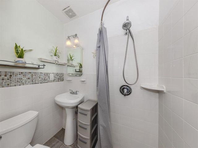 full bath with tile walls, visible vents, toilet, wainscoting, and tiled shower