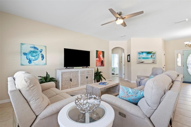 living area featuring arched walkways, light tile patterned flooring, ceiling fan with notable chandelier, visible vents, and baseboards