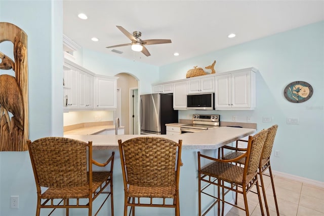 kitchen featuring arched walkways, light countertops, appliances with stainless steel finishes, white cabinets, and a peninsula