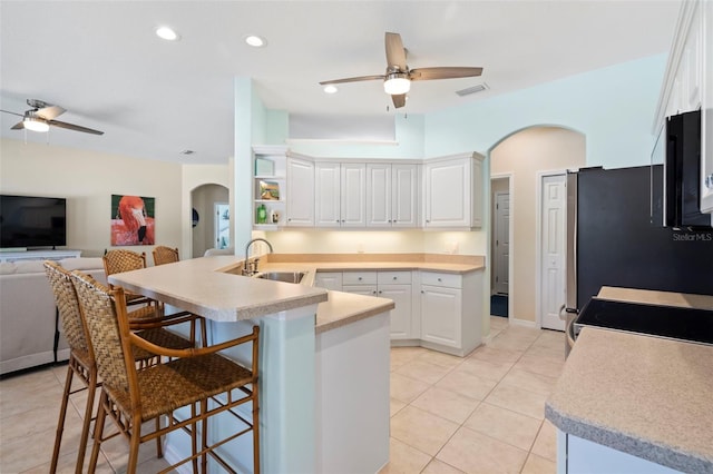 kitchen featuring arched walkways, light countertops, white cabinets, a sink, and a peninsula