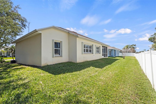 rear view of house featuring stucco siding, fence, and a yard