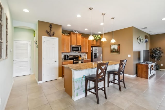 kitchen featuring visible vents, light stone countertops, a kitchen island with sink, stainless steel appliances, and backsplash