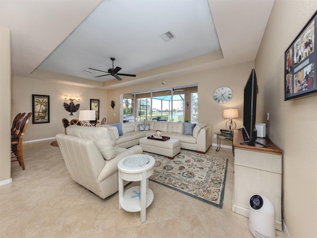 living room with a raised ceiling, visible vents, ceiling fan, and baseboards