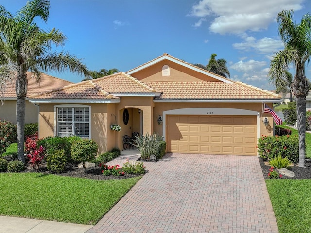 mediterranean / spanish-style house featuring an attached garage, a tiled roof, decorative driveway, and stucco siding