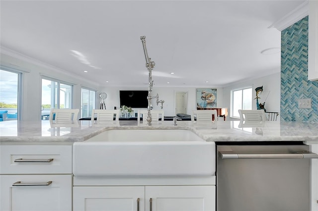 kitchen with light stone counters, stainless steel dishwasher, ornamental molding, white cabinets, and a sink