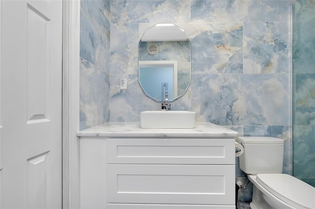 bathroom with toilet, vanity, and tile walls