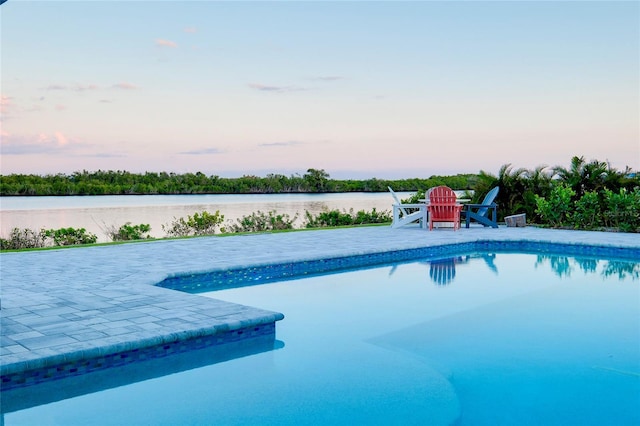 pool at dusk with a patio area, a water view, and an outdoor pool