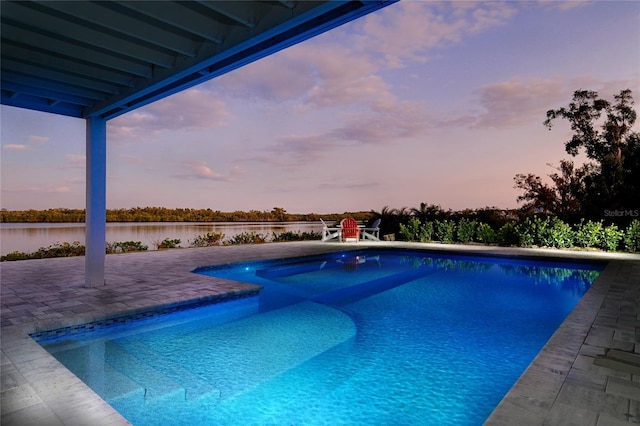 pool at dusk featuring a water view, an outdoor pool, and a patio