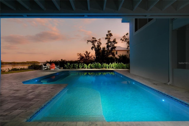 pool at dusk featuring a patio area, a water view, and an outdoor pool