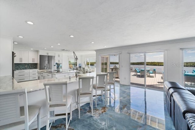 kitchen featuring tasteful backsplash, a kitchen breakfast bar, freestanding refrigerator, light stone countertops, and white cabinetry