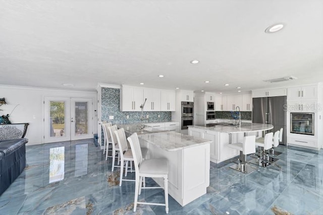 kitchen featuring appliances with stainless steel finishes, marble finish floor, a large island with sink, a kitchen bar, and white cabinetry