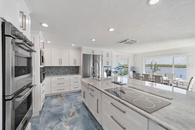 kitchen with tasteful backsplash, white cabinets, appliances with stainless steel finishes, light stone counters, and marble finish floor