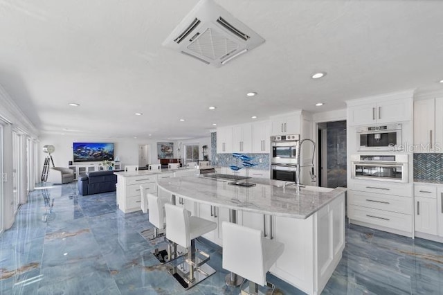 kitchen featuring backsplash, stainless steel double oven, open floor plan, a large island with sink, and a peninsula