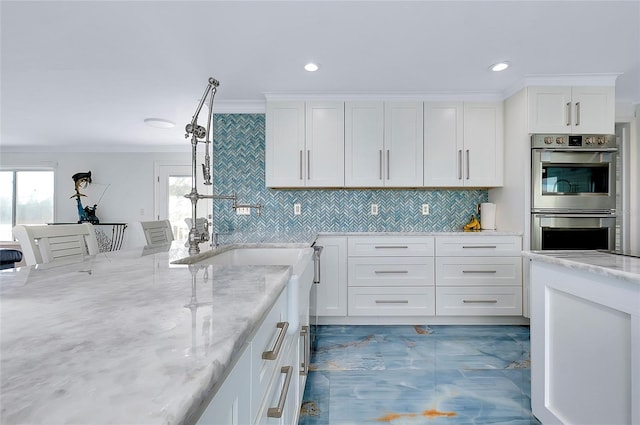 kitchen featuring double oven, light stone counters, white cabinets, ornamental molding, and backsplash