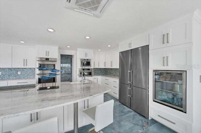 kitchen featuring light stone counters, a breakfast bar, visible vents, appliances with stainless steel finishes, and white cabinets