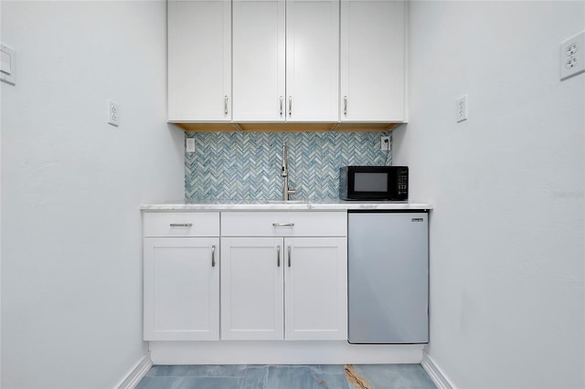 kitchen featuring tasteful backsplash, refrigerator, light countertops, black microwave, and a sink