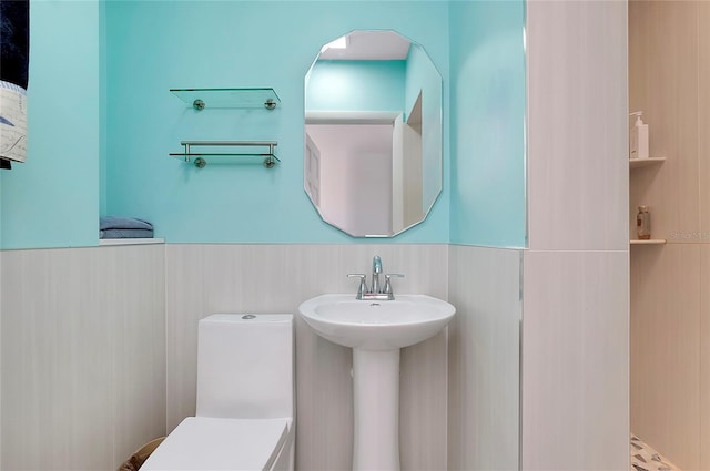 bathroom with toilet, a wainscoted wall, and a sink