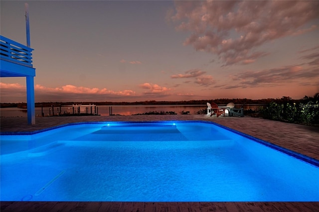 pool at dusk with an outdoor pool, a patio area, and a water view