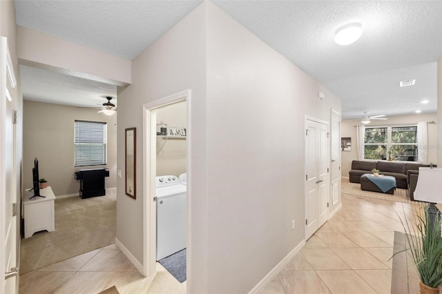 corridor featuring light tile patterned floors, visible vents, a textured ceiling, independent washer and dryer, and baseboards