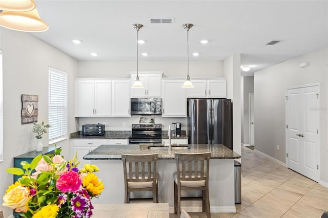 kitchen with stainless steel appliances, an island with sink, visible vents, and white cabinetry