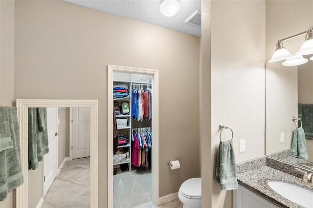 bathroom with visible vents, toilet, tile patterned floors, a spacious closet, and vanity