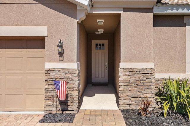 entrance to property with a garage, stone siding, and stucco siding