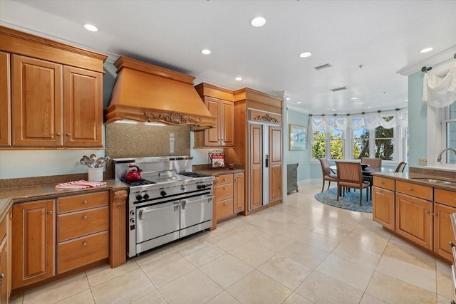 kitchen featuring high quality appliances, brown cabinets, custom exhaust hood, a sink, and recessed lighting