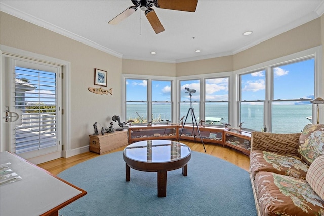 living area with crown molding, a water view, light wood-style floors, a ceiling fan, and baseboards