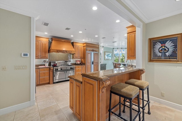 kitchen featuring range with two ovens, a peninsula, a breakfast bar, visible vents, and custom range hood