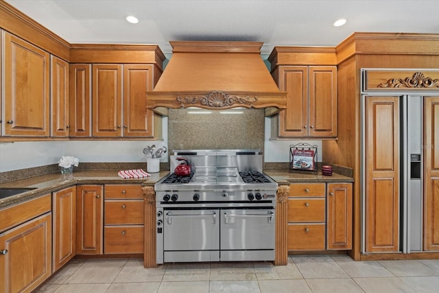 kitchen with premium appliances, recessed lighting, brown cabinetry, light tile patterned flooring, and premium range hood