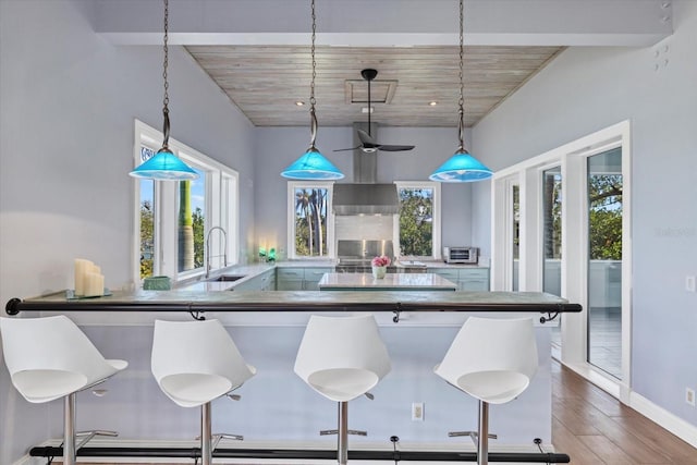 kitchen with wall chimney exhaust hood, a kitchen breakfast bar, wood finished floors, pendant lighting, and a sink