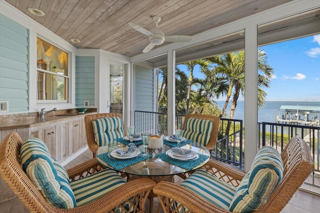 sunroom featuring ceiling fan, a water view, a sink, and wooden ceiling