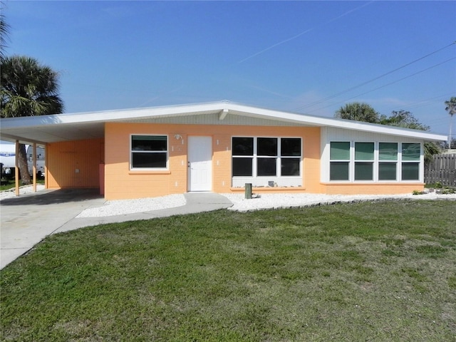 rear view of house with an attached carport, concrete block siding, a yard, and concrete driveway