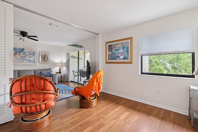 living area featuring a ceiling fan, visible vents, baseboards, and wood finished floors