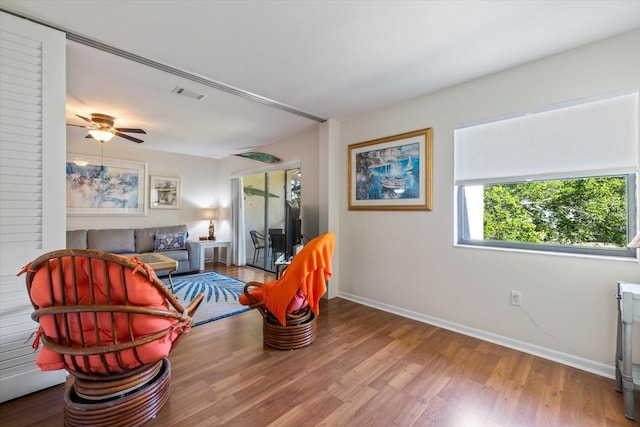 living area with visible vents, ceiling fan, baseboards, and wood finished floors