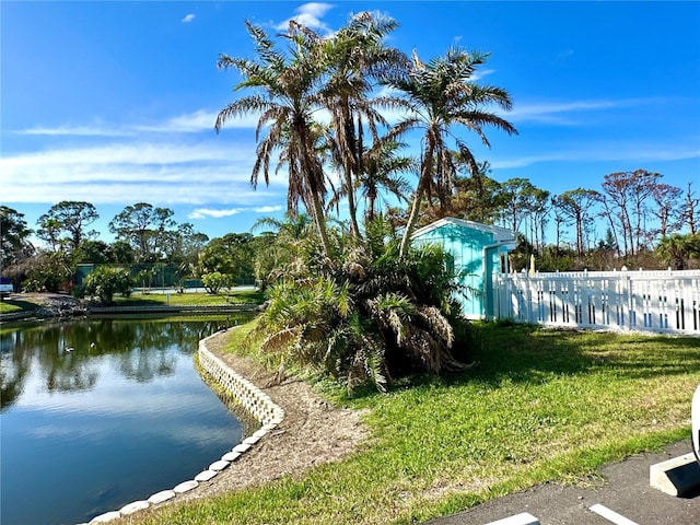 view of property's community with a water view, fence, and a lawn