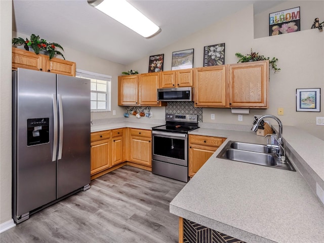 kitchen with light wood finished floors, stainless steel appliances, lofted ceiling, light countertops, and a sink