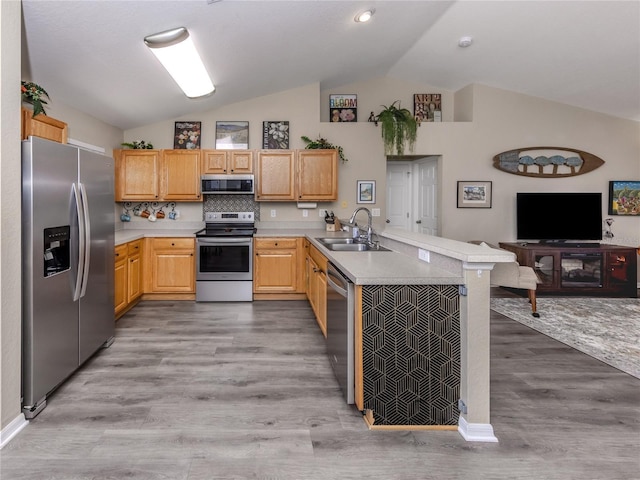 kitchen with light wood finished floors, lofted ceiling, appliances with stainless steel finishes, a peninsula, and a sink