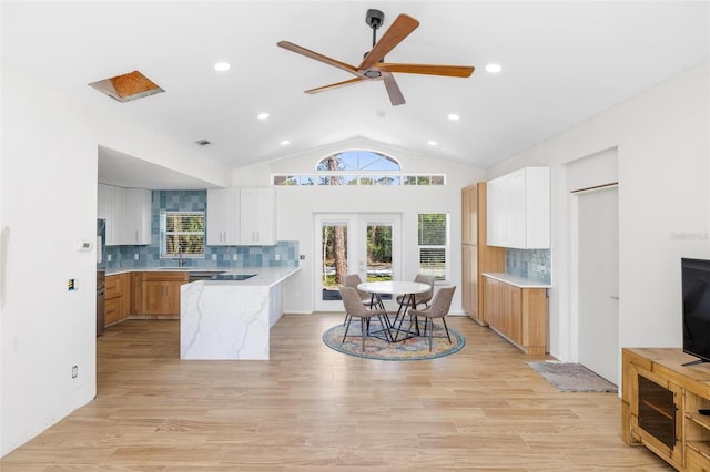 kitchen featuring vaulted ceiling, a peninsula, light wood-style flooring, and white cabinetry