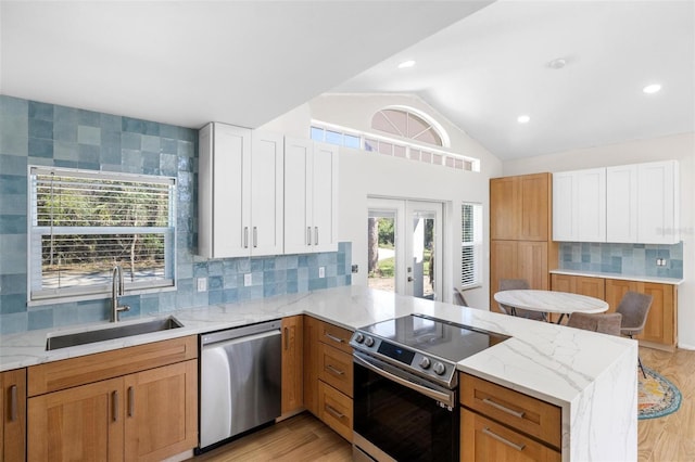 kitchen featuring light stone counters, a peninsula, stainless steel appliances, light wood-type flooring, and a sink