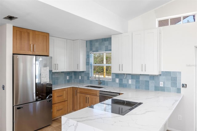 kitchen with a peninsula, light stone counters, stainless steel appliances, and a sink