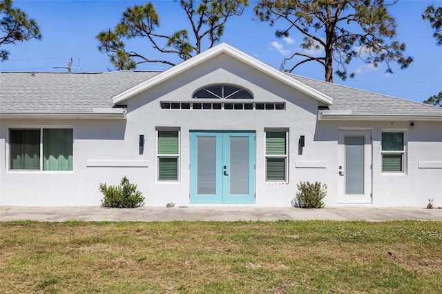 exterior space featuring french doors, a front lawn, a shingled roof, and stucco siding