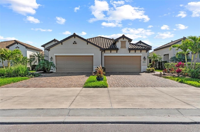 mediterranean / spanish-style house featuring a garage, a tiled roof, decorative driveway, and stucco siding