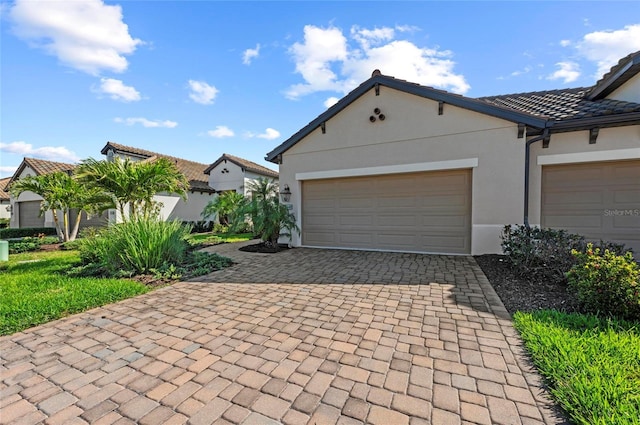 view of front of home featuring decorative driveway, a tile roof, an attached garage, and stucco siding