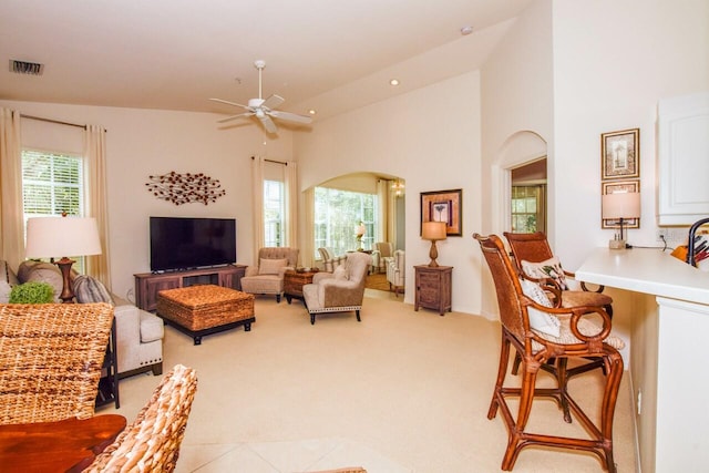 living area featuring arched walkways, recessed lighting, light colored carpet, visible vents, and a towering ceiling