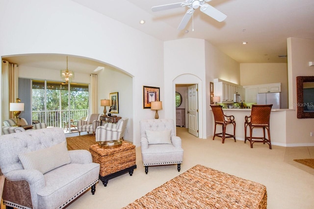 living area featuring arched walkways, light colored carpet, a towering ceiling, ceiling fan with notable chandelier, and recessed lighting