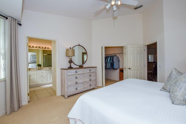 bedroom featuring visible vents, light colored carpet, ensuite bathroom, a walk in closet, and multiple windows